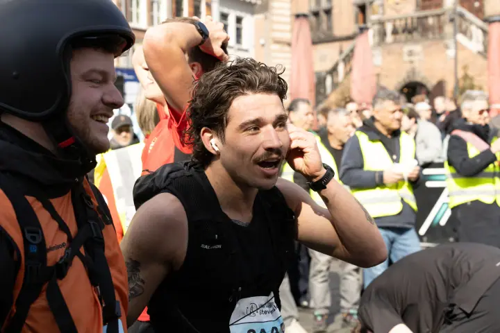 Bezwete finisher met oortjes grijpt naar zijn hoofd van blijdschap, tussen vrijwilligers in gele hesjes