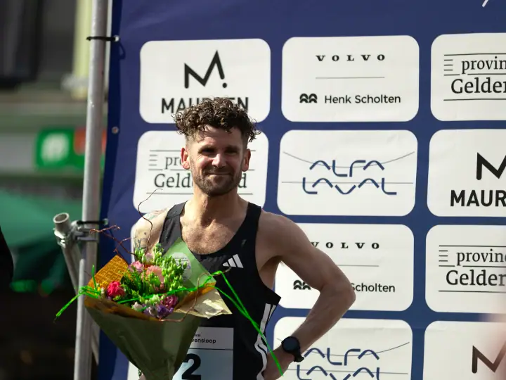 Nummer twee bij de mannen poseert met bloemen voor de sponsorwand van Alfa Laval
