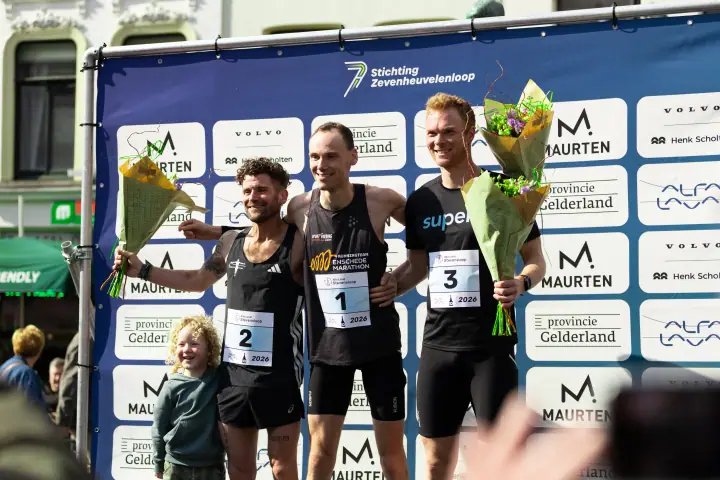Podium bij de mannen van de Stevensloop 2026, de top drie met bloemen en een kind ernaast