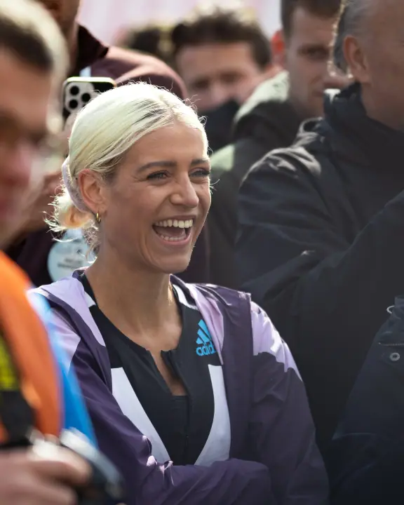 Winnares lacht uitbundig in een paarse trainingsjas tussen het publiek na de wedstrijd