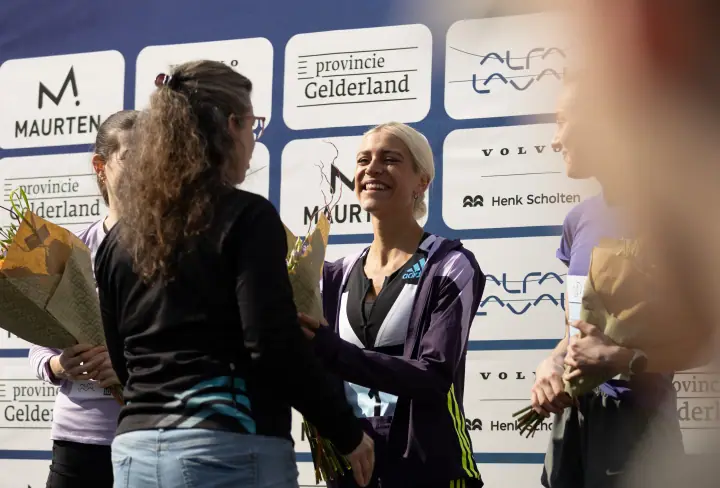 Felicitaties voor de winnares bij het podium, tussen de bloemen en sponsorborden
