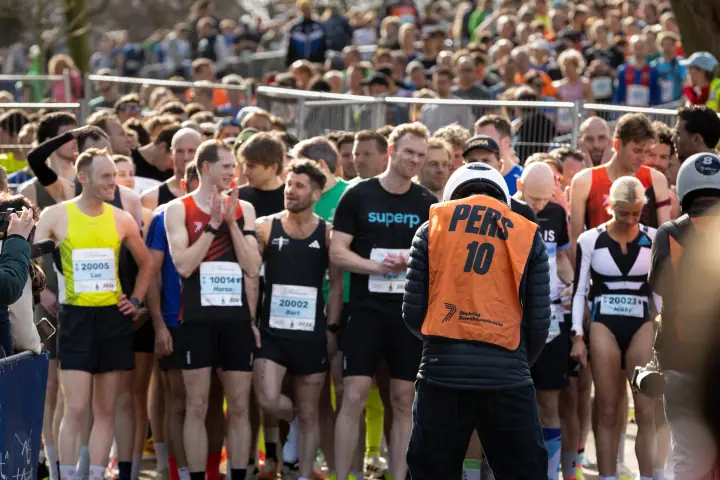 Persfotograaf in oranje hesje staat voor het eliteveld, vlak voor de start
