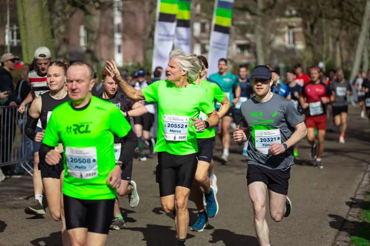 Lopers in felgroene clubshirts rennen door het park, een loper met grijs haar steekt zijn hand op