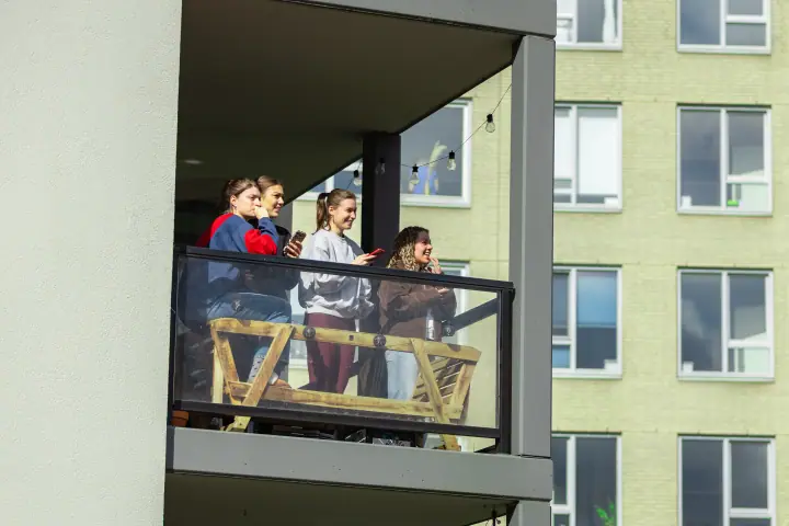 Vier jonge vrouwen volgen de loop vanaf een balkon, telefoon in de hand