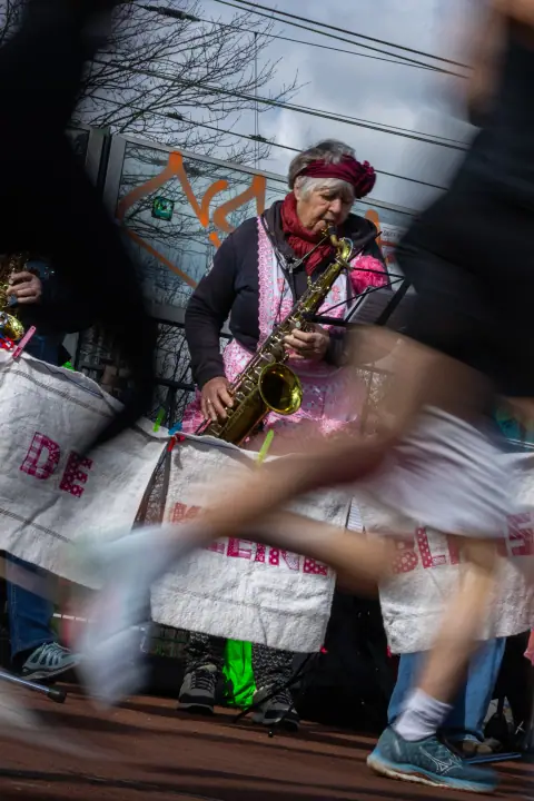 Saxofoniste in roze schort speelt langs de route terwijl een loper voorbij flitst