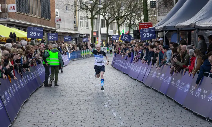 Loper steekt zijn arm in de lucht op de laatste meters, langs rijen publiek in de binnenstad