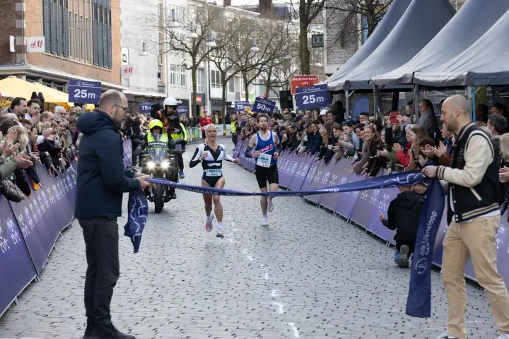 Winnares sprint naar het finishlint dat twee officials klaarhouden, een mannelijke loper vlak achter haar