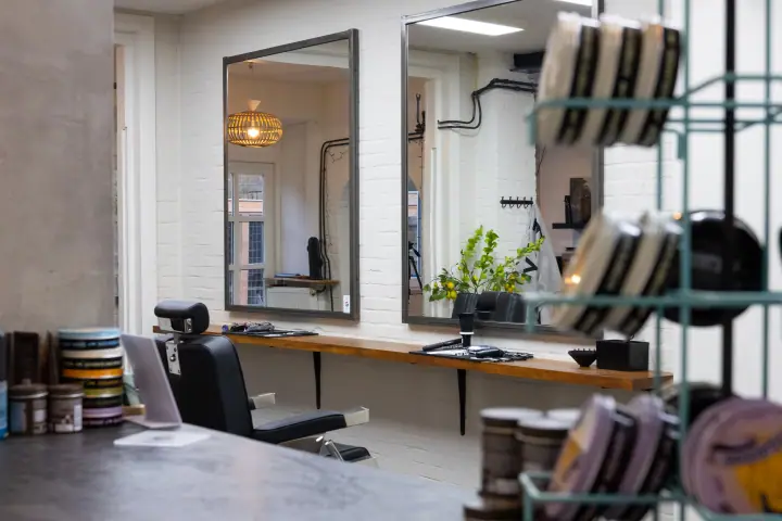 Blik langs een rek met haarproducten naar de spiegels en een kappersstoel