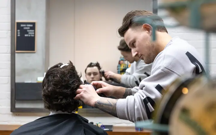 Barbier met getatoeëerde onderarm aan het werk, gespiegeld in de grote wandspiegel