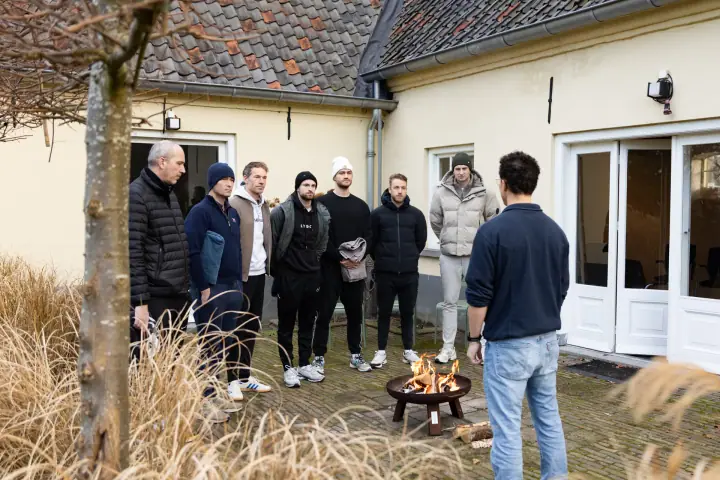 Deelnemers van de Chakana Coaching workshop staan rond een vuurschaal op de binnenplaats van een gele boerderij.
