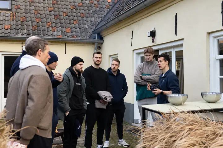 De coach legt de groep iets uit bij een tafel met metalen schalen, vlak voor de ijswateroefening.