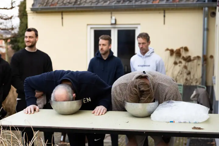 Twee deelnemers duwen hun gezicht in een schaal ijswater terwijl de rest van de groep toekijkt.