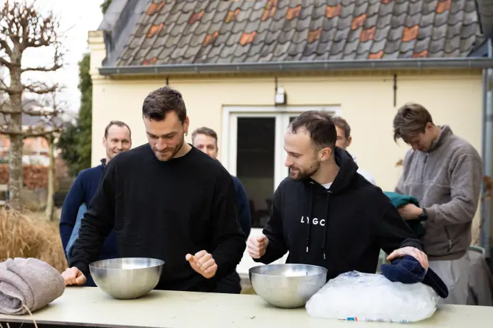 Twee mannen zetten zich lachend schrap boven hun schaal ijswater, naast een zak ijsblokjes.