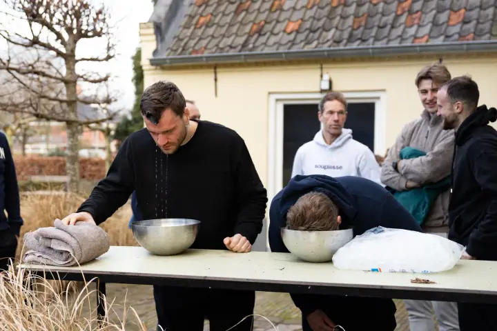 Een deelnemer komt druipend omhoog uit de schaal ijswater, naast hem hangt een ander er nog met zijn gezicht in.