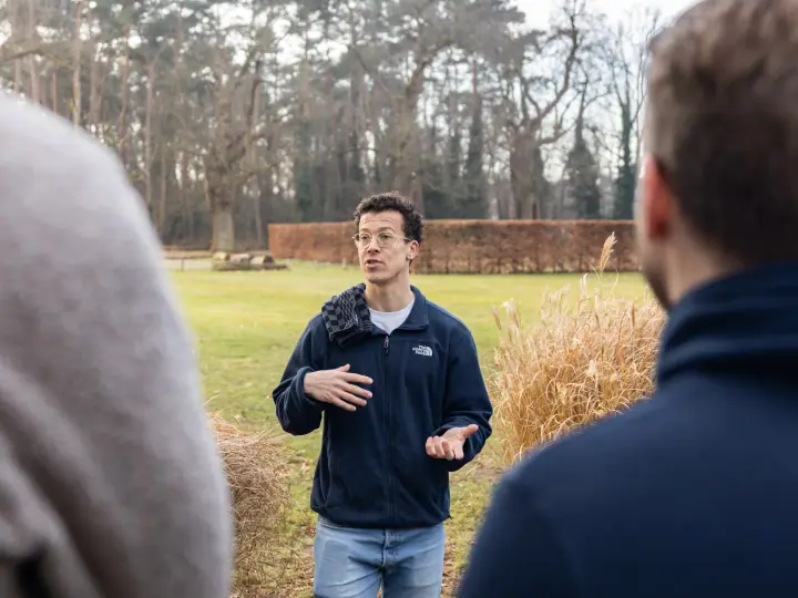 De coach gebaart met beide handen terwijl hij uitleg geeft, tussen twee luisteraars in gefotografeerd.