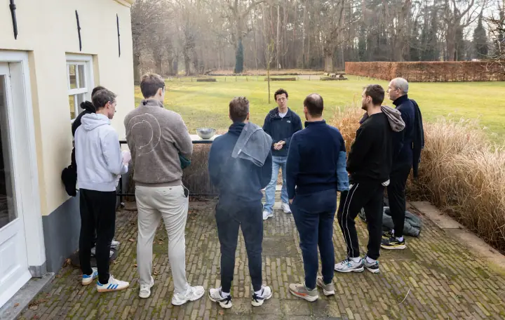 Overzichtsfoto van de groep op het terras die luistert naar de coach aan de rand van het gazon.