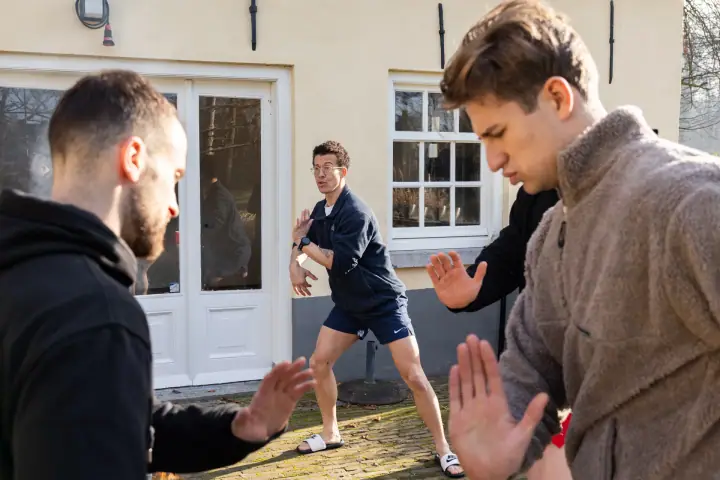 Geconcentreerde gezichten tijdens een bewegingsoefening op het terras, de handen naar voren gestrekt.