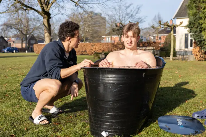 Een jonge deelnemer houdt de rand van het ijsbad vast, de coach moedigt hem van dichtbij aan.