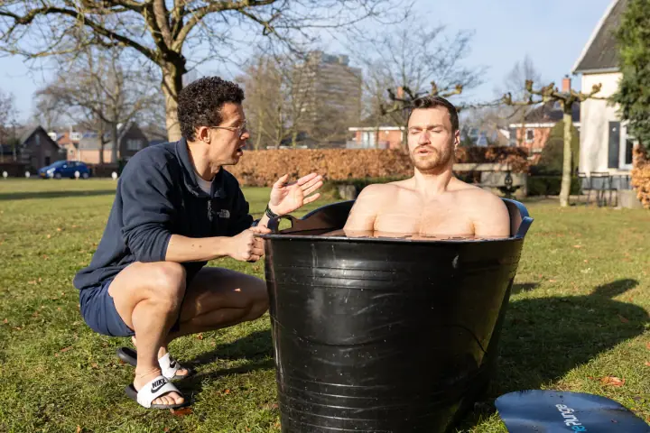 Met gesloten ogen zit een deelnemer in het koude water terwijl de coach hem instructies geeft.