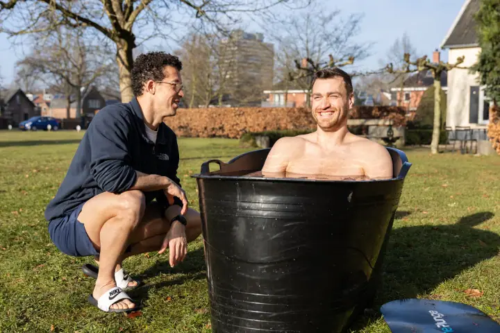 Brede grijns in het ijsbad tijdens de Chakana Coaching workshop, de coach lacht ernaast.