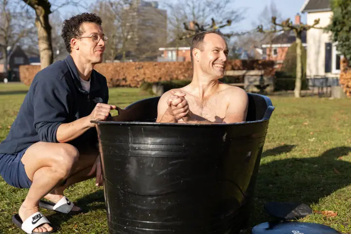 Ontspannen glimlach van een deelnemer in het ijsbad, handen ineen, met de coach aan de rand.