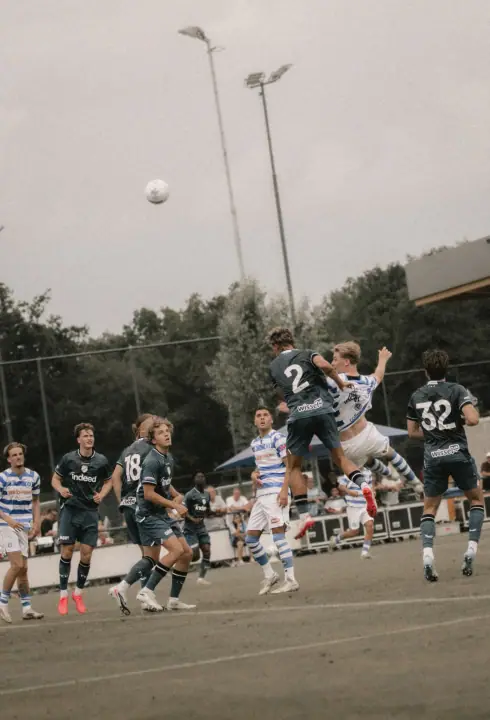 Kopduel hoog in de lucht tussen spelers van De Graafschap en tegenstanders in donkerblauw