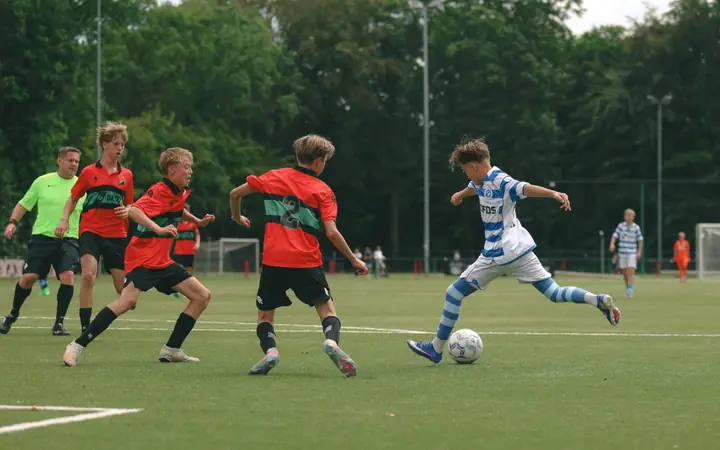 Jonge speler van De Graafschap dribbelt op drie spelers van NEC af, met de scheidsrechter erachter