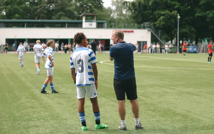 Trainer geeft speler nummer 3 aanwijzingen langs de lijn tijdens een jeugdwedstrijd