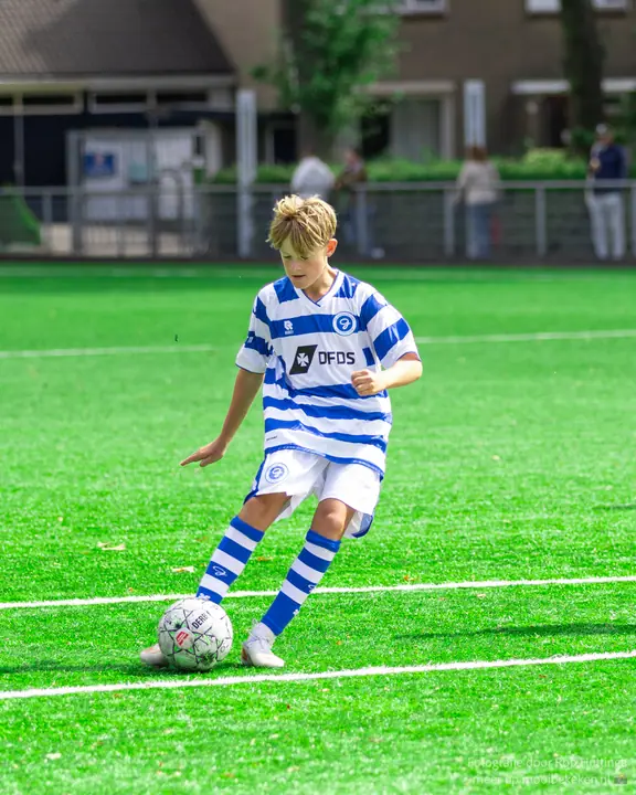 Blonde jeugdspeler van De Graafschap speelt de bal geconcentreerd breed met de binnenkant voet