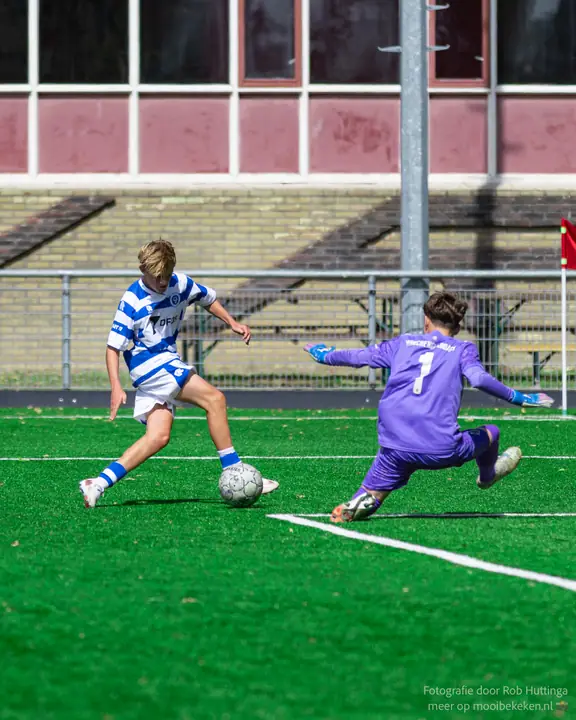 Keeper in paars duikt uit naar de voeten van een aanvaller van De Graafschap