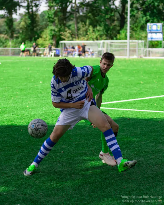 Jeugdspeler van De Graafschap schermt de bal af met zijn lichaam tegen een speler in groen