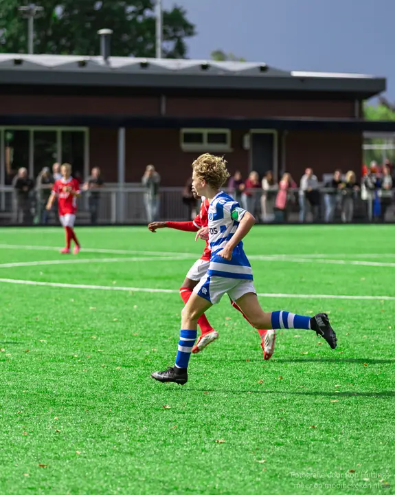 Speler met blonde krullen sprint terug voor De Graafschap, een tegenstander in rood op zijn hielen