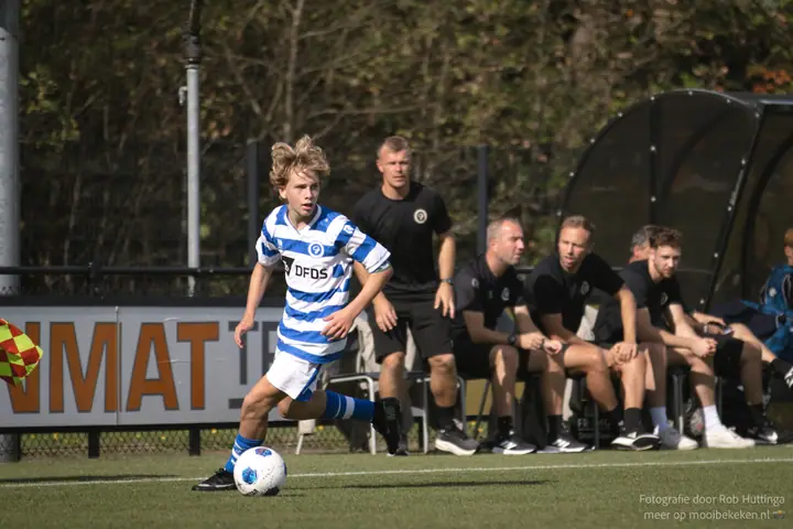 Jeugdspeler van De Graafschap dribbelt langs de lijn, met de staf van Vitesse op de bank
