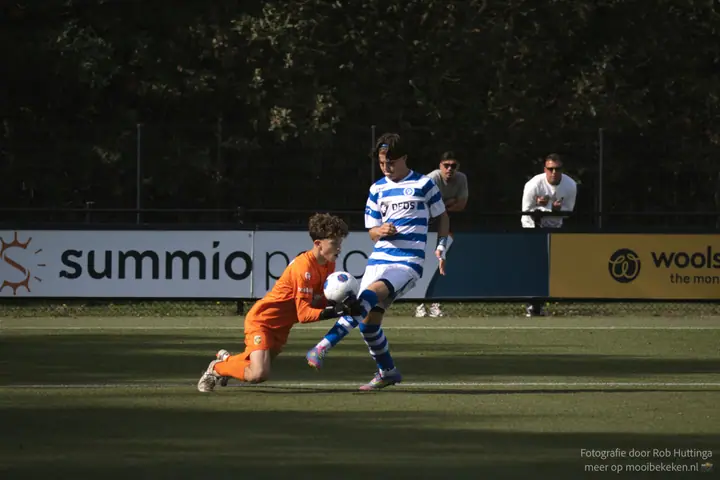 Keeper in oranje pakt de bal voor de voeten van een aanvaller van De Graafschap weg