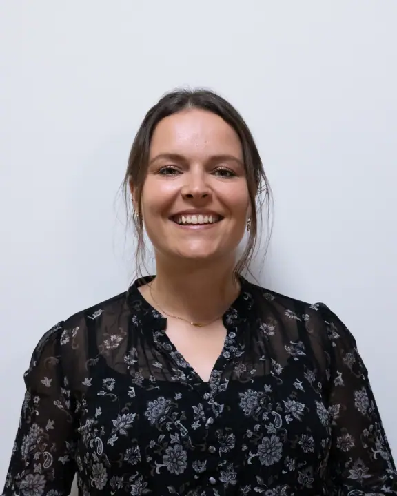 Portret van een lachende vrouw met opgestoken haar in een zwarte blouse met bloemenprint