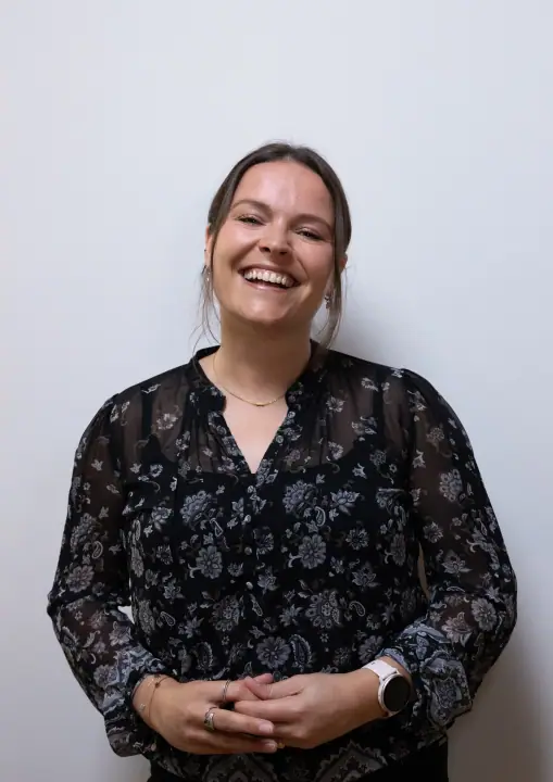 Vrouw in zwarte bloemenblouse lacht breed met haar handen voor zich gevouwen
