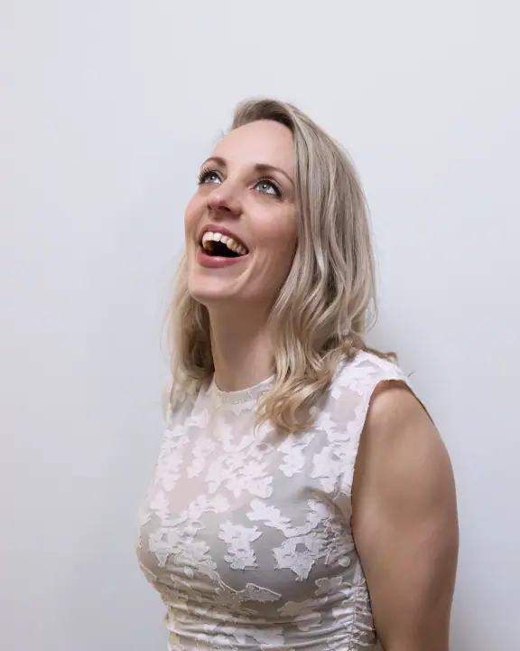 Blonde vrouw in een wit kanten topje kijkt lachend omhoog, portret uit de businessshoot voor Milou
