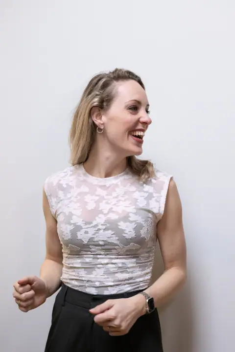 Spontaan portret van een blonde vrouw die lachend opzij kijkt, in kanten top en zwarte broek