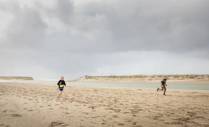 Een kind en een volwassene rennen over een leeg strand onder zware donkere wolken.