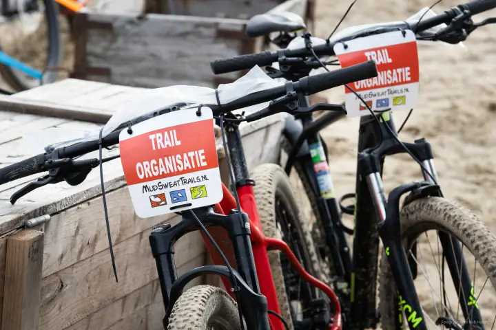 Mountainbikes met bordjes Trail Organisatie van MudSweatTrails.nl staan klaar op het strand.