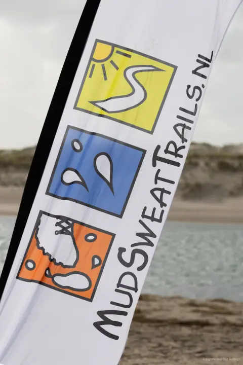 Beachvlag van MudSweatTrails.nl met het logo van een zon, zweetdruppels en een modderige schoen.