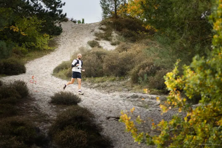 Sportfotografie bij Mudsweattrail 2025, een loper daalt een zandpad af door heide en herfstkleurige struiken.