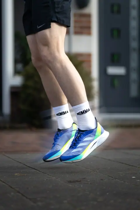 Hardloper springt omhoog in NIMMA sokken en blauwe schoenen, met een creatief bewegingseffect