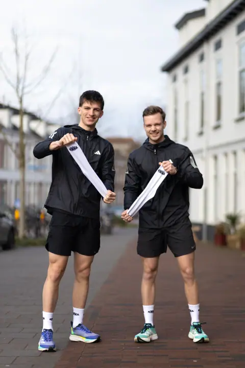 Staand portret van twee lachende lopers met uitgerekte NIMMA sokken tussen hun handen