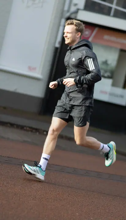 Lachende hardloper in zwart jack rent door de straat, sportfotografie voor Nimma Running Club