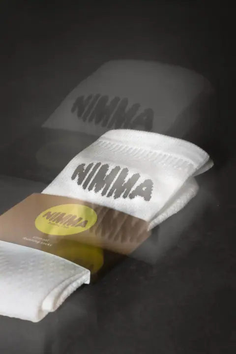 Opgevouwen NIMMA sokken met een spookachtige dubbele afdruk van het logo op een donkere ondergrond