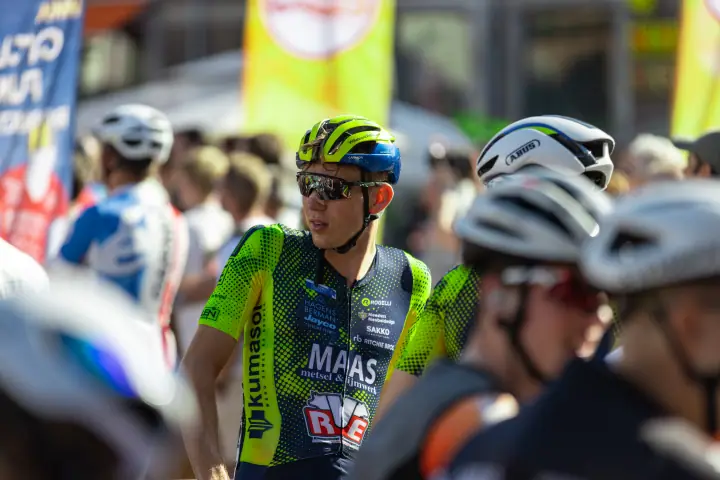 Renner in fluogeel teamshirt met zonnebril kijkt om zich heen tussen het startveld