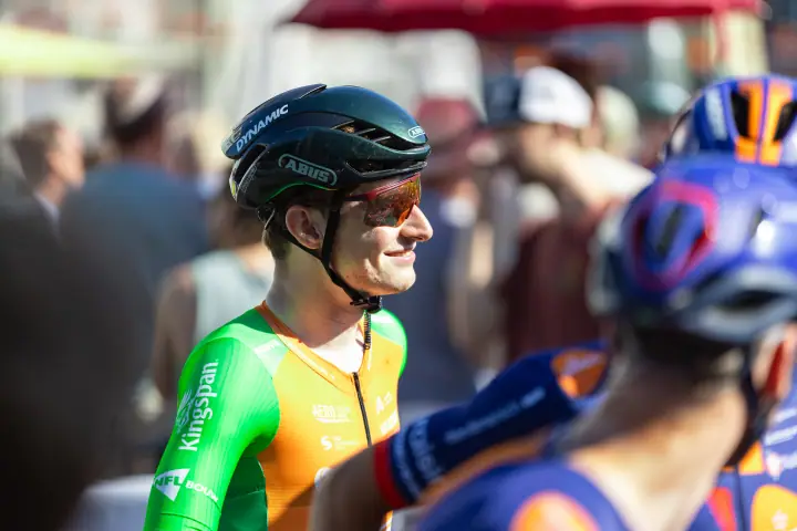 Lachende renner in groen-oranje Kingspan-shirt kijkt opzij in de drukte voor de start