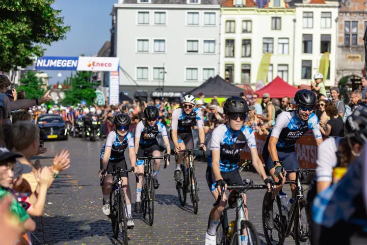 Toeschouwers klappen voor renners in blauw-witte teamshirts die door het centrum van Nijmegen rijden