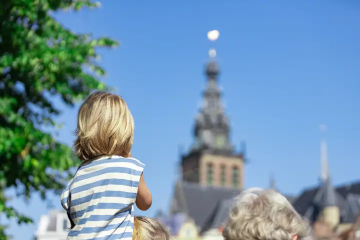 Kind op de schouders kijkt naar de toren van de Stevenskerk tegen een strakblauwe lucht